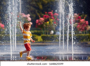 excited redhead baby boy having fun between water jets, in fountain. Summer in the city