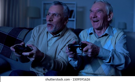 Excited retired men playing video game at night together, friendship connection