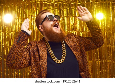 Excited rich redhead man in bling golden neck chain and cool glasses DJing and having fun at glamour party. Happy fashionable showman with beard and handlebar mustache singing and dancing on stage