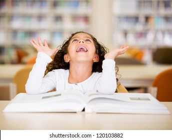 Une écolière excitée à la bibliothèque lisant un livre : photo de stock