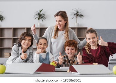 excited schoolkids and teacher showing thumbs up in classroom - Powered by Shutterstock