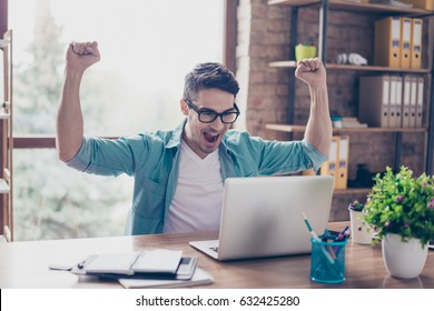 Excited Screaming Young Man Looking At The Screen Of His Computer And Triumphing With Raised Hands