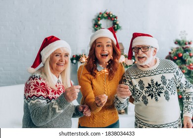 excited senior couple with daughter in santa hats holding sparklers on christmas - Powered by Shutterstock