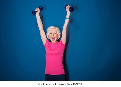 Excited Senior Fitness Woman Training With Dumbbells Isolated On Blue 