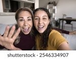 Excited senior Latin mother and beautiful adult daughter posing for close up portrait, taking selfie, laughing and shouting for joy, singing song together, looking at camera with toothy smile