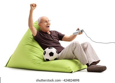 Excited Senior Man Playing A Soccer Videogame Seated On A Green Beanbag Isolated On White Background