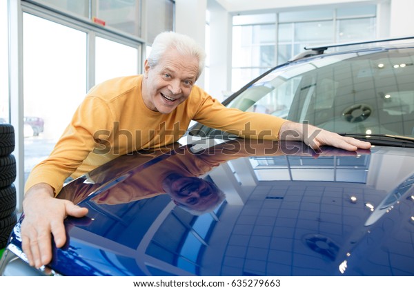 Excited senior man smiling joyfully\
hugging his newly bought automobile at car dealership copyspace\
offer discount selling price insurance rental travelling retiring\
retirement sales\
transportation