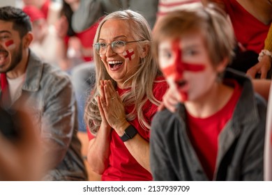 Excited senior woman football fan supproting English national team in live soccer match at stadium.