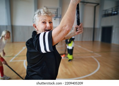 Excited Senior Woman Playing Floorball In Gym With Her Friends.