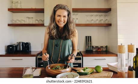 Excited senior woman smiling cheerfully while having some delicious vegan food. Mature woman serving herself a healthy buddha bowl at home. Woman taking care of her aging body with a plant-based diet.