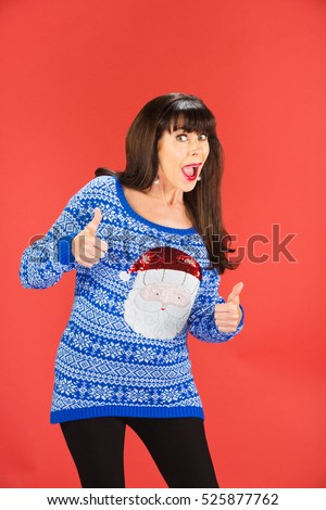 Excited single woman in tacky Christmas sweater with thumbs up over red background