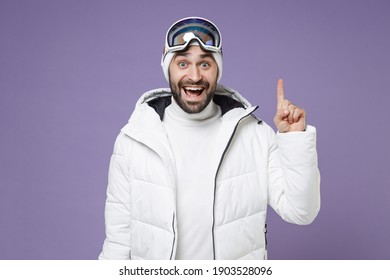 Excited skier man in white windbreaker jacket ski goggles mask hold index finger up with great new idea spend weekend winter in mountains isolated on purple background. People lifestyle hobby concept