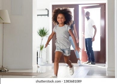 Excited Small Funny African American Girl Run In Hallway, Coming Home With Mom And Dad, Happy Little Kid Have Fun In Corridor Returning To Own House With Young Parents. Family Mortgage Concept