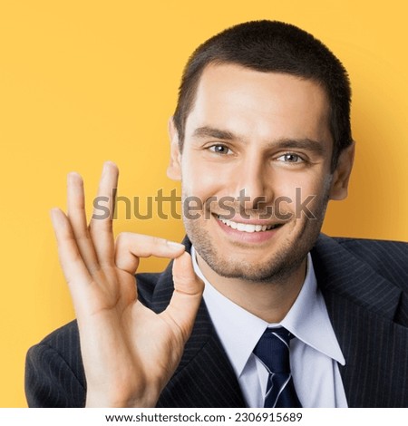Excited smile positive businessman wear black confident suit show make ok okay hand sign, isolated orange yellow color background. Happy gesturing brunette man. Business success concept. Square photo