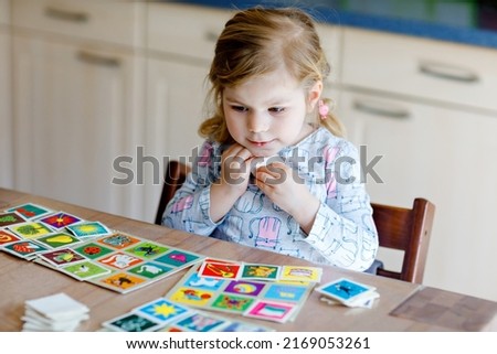 Excited smiling cute toddler girl playing picture card game. Happy healthy child training memory, thinking. Creative indoors leisure and education of kid. Family activity at home.