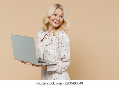 Excited Smiling Elderly Gray-haired Blonde Woman Lady 50s Years Old Wears Pink Dress Hold Use Work On Laptop Pc Computer Looking Back Behind Isolated On Plain Pastel Beige Background Studio Portrait