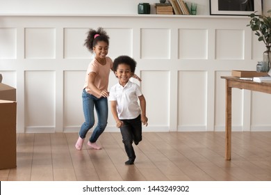 Excited smiling preschooler kids run in new empty home feel happy to move, overjoyed small brother and sister laugh have fun chasing each other playing in living room together. Entertainment concept
