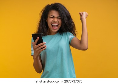 Excited soccer fan girl cheering for favourite team and making winner gesture with her fist being happy about the score. Young woman showing sincere excitement about the victory in online lottery.  - Shutterstock ID 2078737375