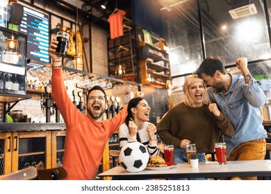 Excited soccer fans celebrating while watching soccer match on TV in bar. - Powered by Shutterstock