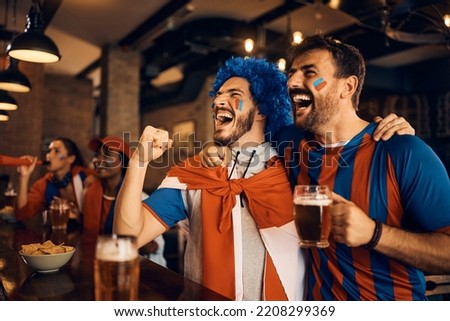 Excited soccer fans celebrating while watching soccer match on TV during the world cup in bar.