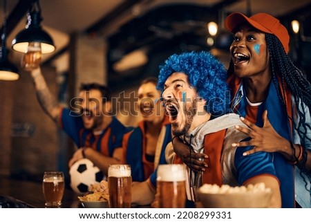 Excited sports fans watching football match on TV and shouting after the winning goal of their favorite team during the world cup.