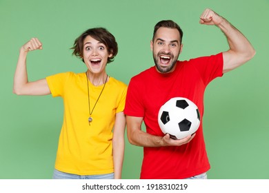 Excited Strong Couple Friends Sport Family Woman Man Football Fans In Yellow Red T-shirts Cheer Up Support Favorite Team With Soccer Ball Showing Biceps Muscles Isolated On Green Background Studio