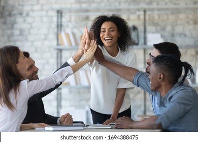 Excited successful african american businesswoman with multiracial business people giving high five, celebrating win. Happy employees team engaged in team building activity at corporate meeting.