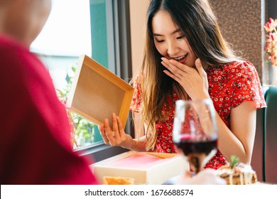 Excited Surprise Asian Woman On Red Dress Opening The Present Gift Box That She Got It From Her Boyfriend.