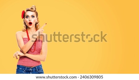 Excited surprised, astonished or very happy blond woman. Pin up girl open mouth pointing away side by finger. Beauty model showing indicate click copy space. Retro vintage concept image. Yellow color.