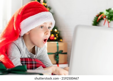 Excited surprised boy in a red Santa hat looks at the laptop screen. A shocked child lies at home in front of the Christmas tree. Merry Christmas online shopping, sale season. - Powered by Shutterstock