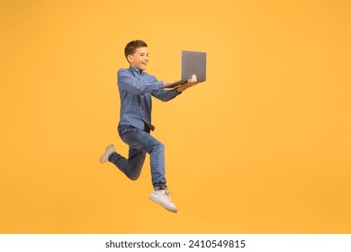 Excited Teen Boy With Laptop Computer In Hands Jumping On Yellow Background, In Motion Shot Of Happy Male Teenager Looking At Device Screen With Interest, Enjoying Online Offer, Full Length - Powered by Shutterstock