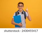 Excited Teen Boy Wearing Eyeglasses Having Idea, Raising Finger Up, Clever Teenage Male Child Holding Books, Ready To Answer A Question, Standing On Yellow Studio Background, Copy Space