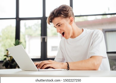 Excited Teen Boy In White T-shirt Using Laptop At Home