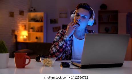 Excited teenage boy playing computer game and eating snack, leisure activity