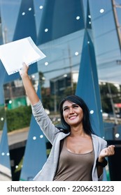 Excited Thai Woman Celebrating Holding Up Documents Outside Financial Building. Smiling Transgender Person Acting Exultant Holding Files. Bank Loan Approval, Test Passed Concepts