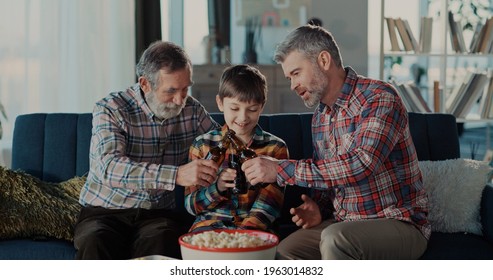 Excited Three Generation Men Family Grandson Young Father And Old Grandfather Fans Hold Soccer Ball Remote Control Watch Tv Sport Game Celebrate Goal Television Team Victory In Tv Match Sit On Sofa