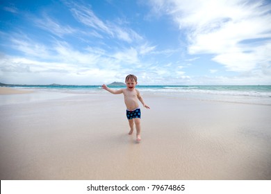 Excited Toddler Running Away From The Waves Towards The Camera On A Tropical Beach