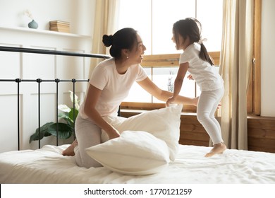 Excited vietnamese ethnicity female family in pajamas having fun on comfortable bed, playing pillow fight, enjoying energetic morning time after waking up together, laughing joking in bedroom. - Powered by Shutterstock