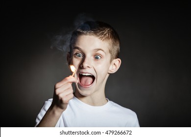 Excited Wide Eyed Male Child Wearing White Shirt Yelling With Flaming Match Against A Black Background