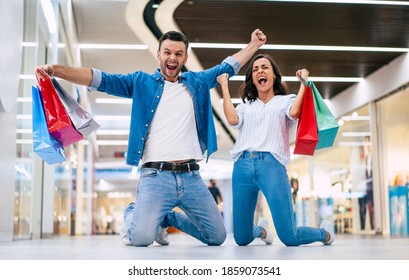  Excited Winning Couple In Love Or Family With Paper Bags In Hands While Are Shouting During Shopping In The Mall