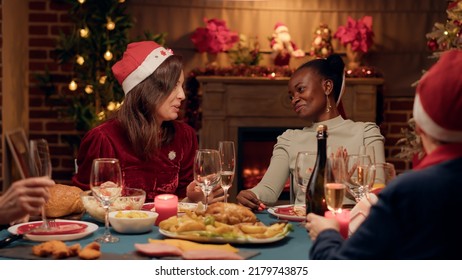 Excited woman discussing with close friend at Christmas dinner while drinking champagne. Festive diverse people celebrating winter feast with sparkling wine and traditional home cooked food. - Powered by Shutterstock