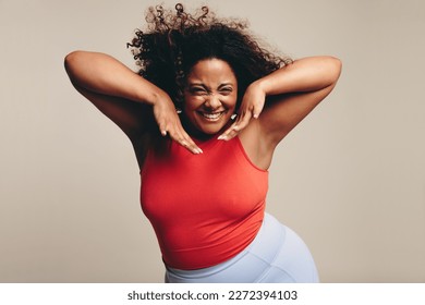 Excited woman with a fit and curvy form having a great time in a lively dance workout. She celebrates her body, proudly showing her confidence as she expresses herself through body movement.