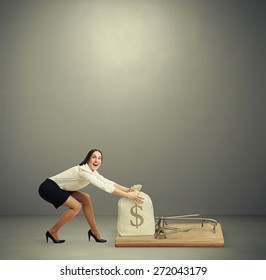 Excited Woman In Formal Wear Reaching Her Arms To Take Bag With Money In Big Mousetrap Over Dark Grey Background With Empty Copyspace Overhead