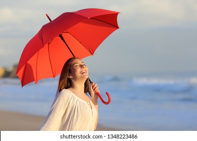 Excited Woman Holding Red Umbrella Celebrating Success On The Beach At Sunset