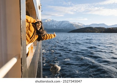 Excited woman leans out of a ferry, enjoying the fresh air and breathtaking snowy mountain scenery. - Powered by Shutterstock