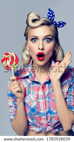 Excited woman with lollipop, dressed in Pinup style. Blond model in retro fashion and vintage concept studio shoot. Surprise or Shock emotion. Vertical banner composition. Studio image.