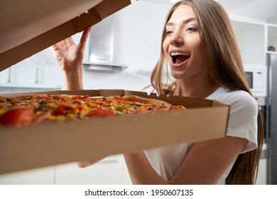 Excited Woman Opening Box With Pizza At Home. Concept Of Lunch And Dinner In Kitchen.