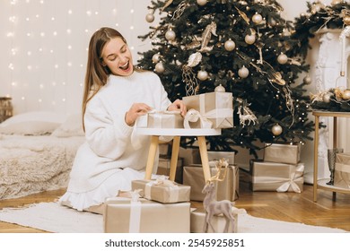 Excited woman opening christmas gifts near a decorated christmas tree, enjoying the festive atmosphere - Powered by Shutterstock