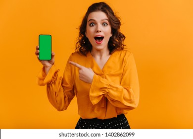 Excited Woman Pointing With Finger At Digital Device. Studio Shot Of Shocked Girl Holding Smartphone With Blank Screen.