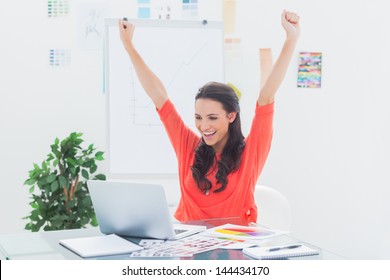 Excited woman raising her arms while working on her laptop in her office - Powered by Shutterstock